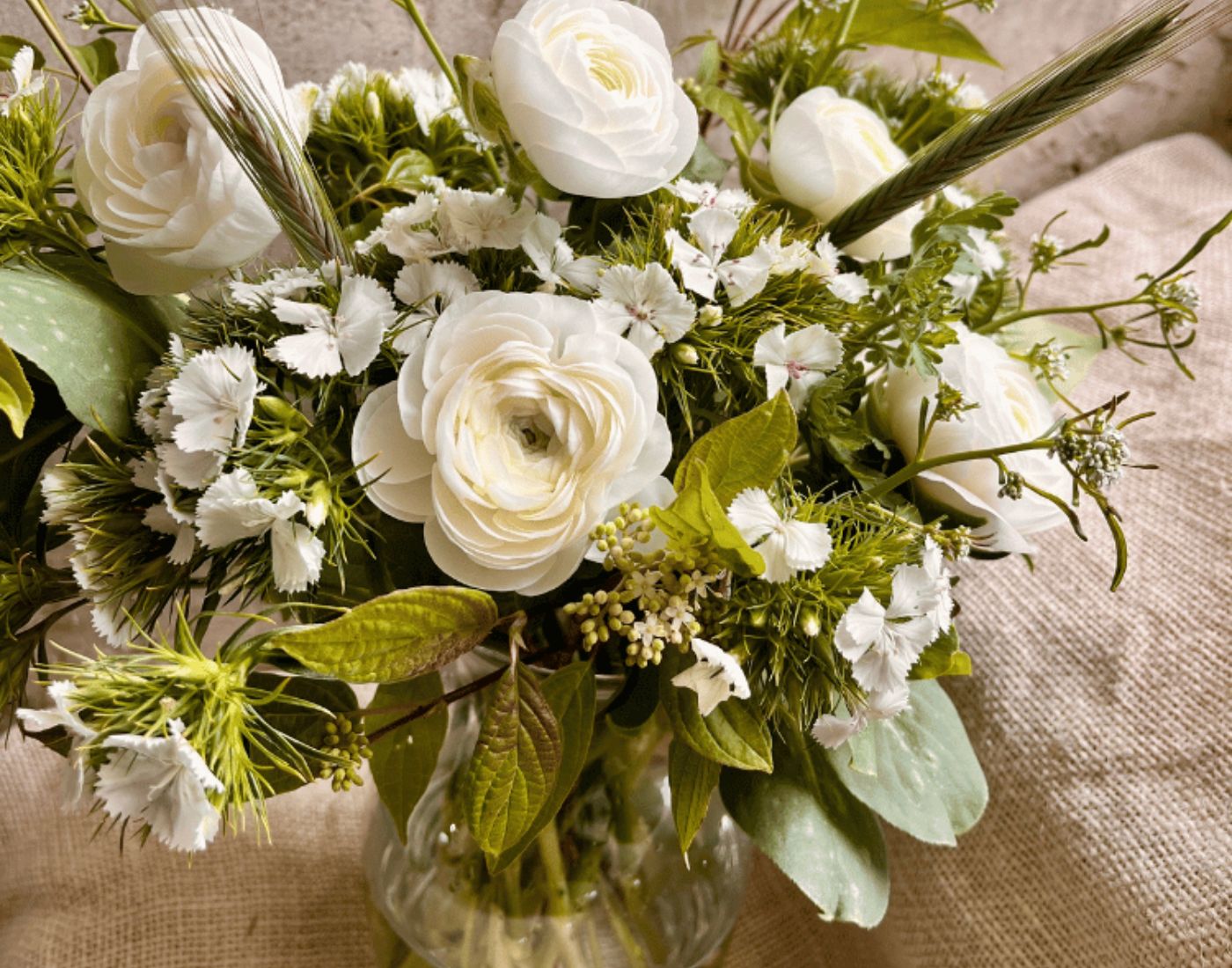 All-white funeral arrangement of ranunculus with green rye grass, grown in West Bend, Wisconsin